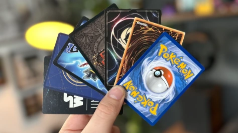 A hand holding a fan of various trading cards including Pokémon, Yu-Gi-Oh!, and Star Wars Unlimited.